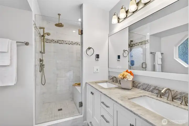 The beautifully remodeled primary bath is a standout feature of this home, showcasing a frameless glass shower with tile surround, rain head fixture, dual undermount sinks with marble countertops, and heated floors — a spa-quality upgrade that transforms the daily routine into something you look forward to.
