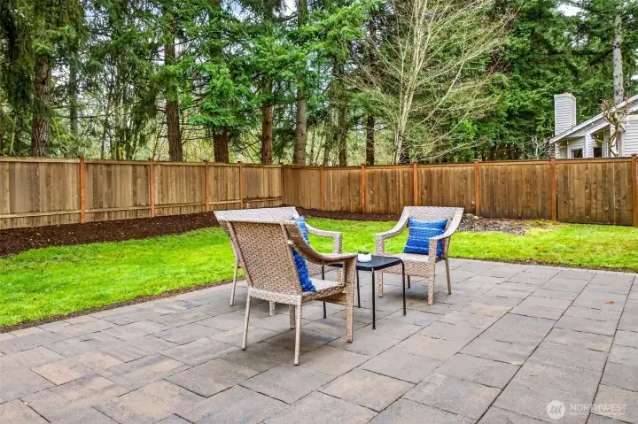 The spacious paver patio offers a private outdoor living space wrapped in the sights and sounds of the Pacific Northwest, with a fully fenced yard, lush lawn, and a towering backdrop of mature evergreens that create a natural sense of seclusion and serenity.