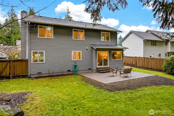 The fully fenced backyard is generously scaled and beautifully framed by mature Pacific Northwest evergreens, offering a private outdoor sanctuary with a paver patio, open lawn, and easy indoor-outdoor flow through the main level sliding doors.