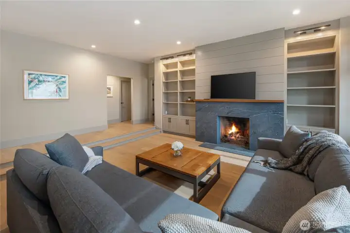 The expansive great room centers on a dramatic stone-surround wood-burning fireplace flanked by custom built-in shelving and cabinetry, creating a cozy yet sophisticated gathering space that perfectly captures the warmth of island life. Wide-plank floors and recessed lighting complete this stunning, move-in-ready living space.