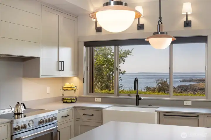 The stunning new kitchen showcases custom shaker cabinetry, crisp stone countertops, a farmhouse apron sink, and professional-grade stainless range — all framed by a wide picture window that keeps Kanaka Bay and the islands in view while you cook.