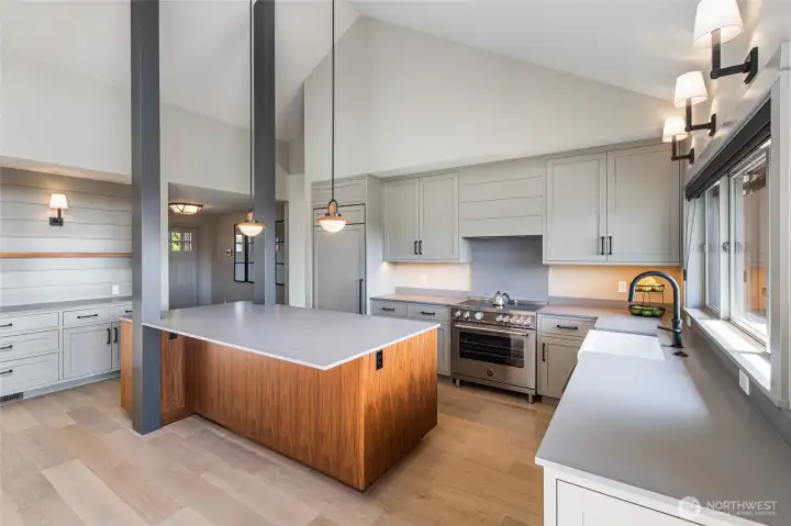 The brand-new chef's kitchen is a showpiece of modern craftsmanship, featuring a striking walnut-wrapped center island with quartz countertops, custom sage-grey shaker cabinetry, and a professional-grade Bertazzoni range beneath soaring vaulted ceilings. Every detail has been curated for both beauty and function, making this the heart of the home.