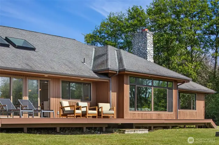 A sprawling wraparound deck with warm cedar siding and floor-to-ceiling windows invites effortless indoor-outdoor living, perfectly framed by the lush Pacific Northwest landscape. The stone chimney and skylights hint at the thoughtful craftsmanship and luxury finishes found throughout this beautifully updated island retreat.