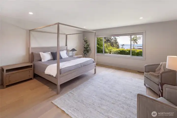 The serene primary suite offers warm hardwood floors, and a large picture window perfectly framing the lush island landscape and sparkling water beyond — a true private retreat.