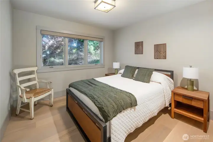 This inviting guest suite with wide-plank hardwood floors and tranquil forest views through a triple window offers a warm, restful escape that effortlessly blends comfort and contemporary island style. Thoughtful finishes and a neutral palette make it easy to imagine waking up here to the sounds of the Pacific Northwest.