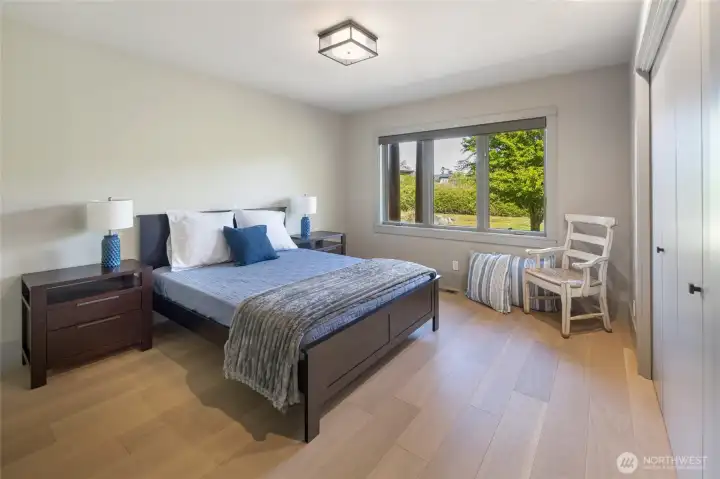 This well-appointed guest bedroom offers a warm and welcoming atmosphere with light hardwood floors, and a bright window overlooking the lush island greenery.