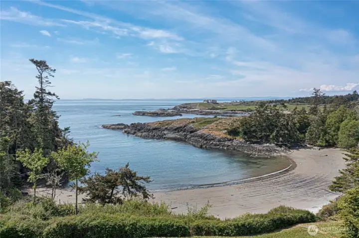Step outside and breathe in the magic of your own sheltered sandy cove, where calm azure waters lap against a gently curved beach framed by wind-sculpted trees and dramatic rock formations — a serene escape just steps from your door.