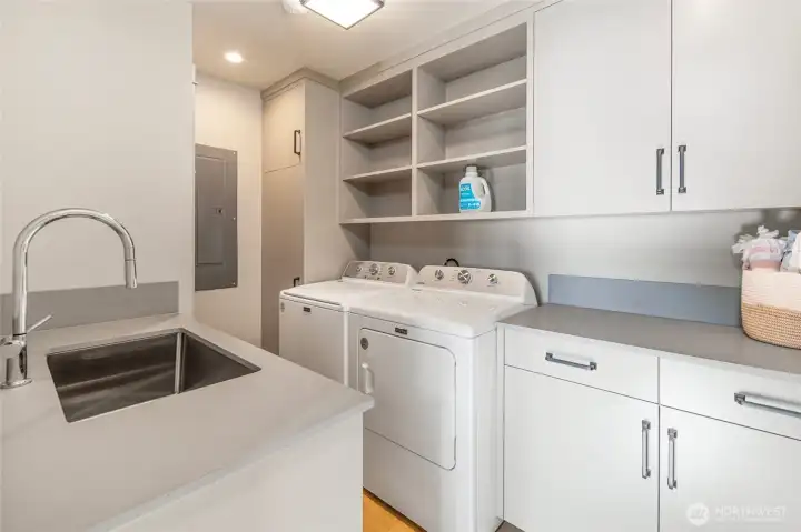 A beautifully appointed laundry room with custom white cabinetry, open shelving, quartz countertops, a deep utility sink, and full-sized Maytag washer and dryer demonstrates the meticulous attention to detail carried throughout every corner of this fully updated home. Practical luxury at its finest.