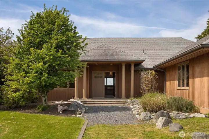 The warm cedar-clad exterior and columned entry portico welcome you with understated Pacific Northwest elegance, set amid lush mature plantings and a natural stone-edged gravel path. This thoughtfully updated single-level home blends seamlessly into its stunning coastal surroundings.