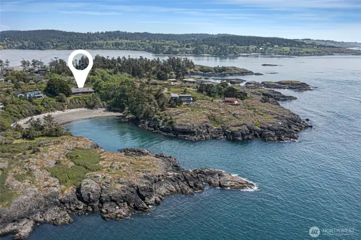 A dramatic aerial perspective from the water looking landward pins the property's coveted position perched above a pristine sandy beach cove, surrounded by wind-sculpted conifers and rugged Pacific Northwest shoreline. This rare vantage captures the true essence of San Juan Island waterfront living at its most spectacular.