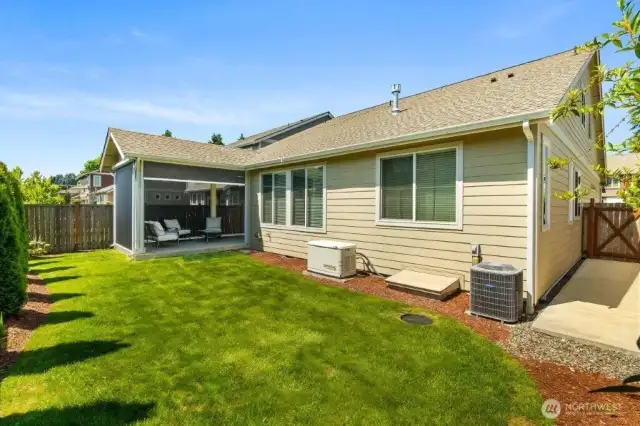 The back yard with extended patio, Generac generator, air conditioning unit, and expanded sidewalk on the far right.
