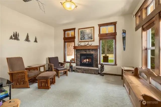 A cozy den is just off of the entry, & hosts a propane fireplace, with wood mantle & rock surround + hearth. This photo showcases the upgraded custom wood wrapped windows & millwork that can be found throughout the home.