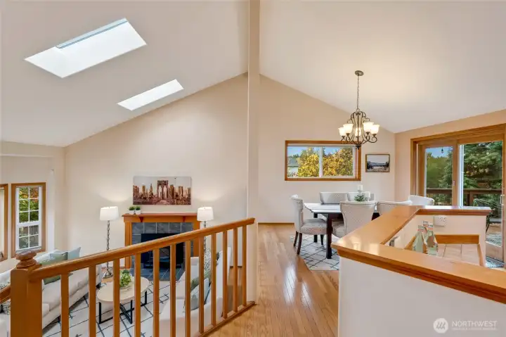 Open-concept dining area overlooking the living room, featuring hardwood floors, vaulted ceilings, and skylights that fill the home with natural light. Ideal layout for entertaining and everyday living.