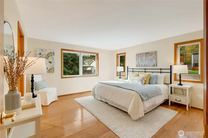 Spacious and serene primary suite with hardwood floors, large windows, and peaceful treetop views. Natural light fills the room, creating a relaxing retreat.