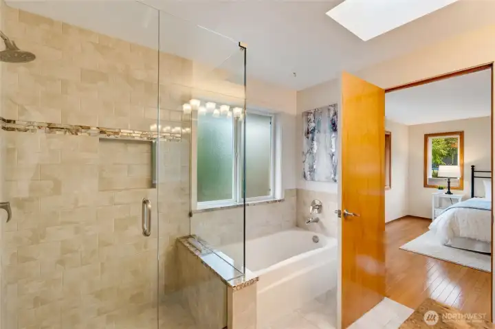 A luxurious spa-inspired layout with a soaking tub, glass-enclosed shower, and elegant finishes throughout. The skylight adds a soft, natural glow to the space.