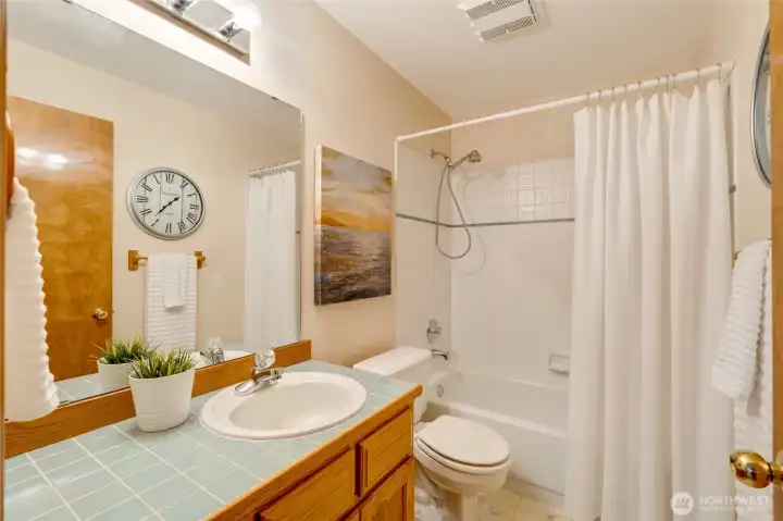 Bright full bath with a tiled tub and shower combination, wood vanity, and coordinating accents. A clean, classic design ideal for guests or secondary use.