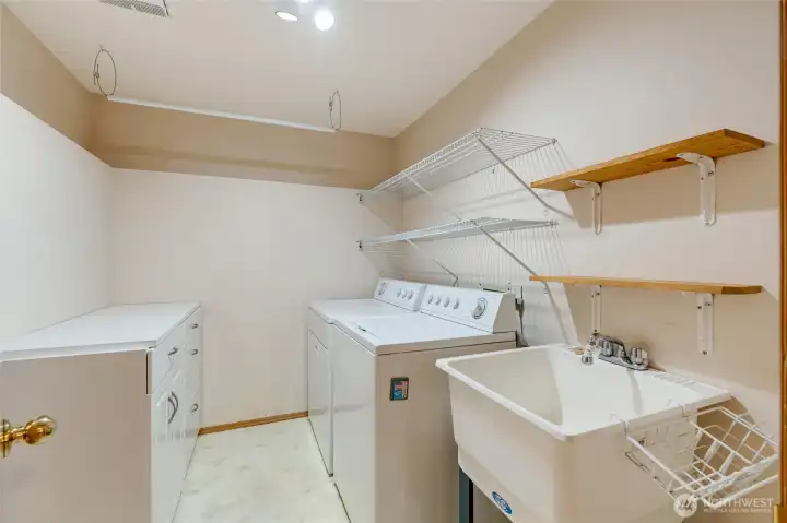 Convenient laundry room with full-size washer and dryer, deep utility sink, built-in shelving, and additional cabinetry for storage and organization.