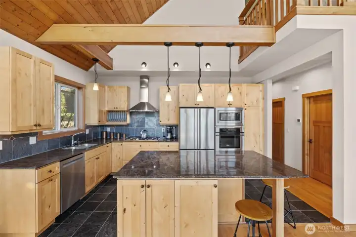Chef’s kitchen with timeless knotty alder  cabinetry, granite counters, and a statement island flows into open-concept living