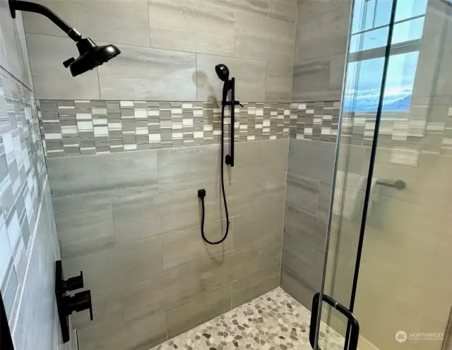 Custom mudpan tile shower with dual valves, glass shelves & sliding glass door.