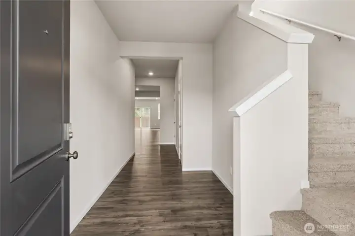 Welcoming entryway featuring a dark front door, long hallway with dark hardwood floors, white walls, and staircase with carpet leading to the upper level. Photos are representative only and may display different color packages and/or upgrades.