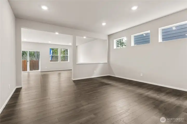 Open great room viewed from the dining area featuring hardwood floors, recessed lighting, three high windows, and a sliding glass door leading to the backyard patio. Photos are representative only and may display different color packages and/or upgrades.