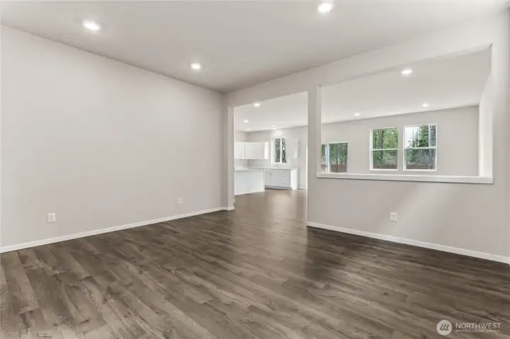 Open-concept great room with hardwood floors, neutral walls, recessed lighting, and a large window with natural backyard views, with an open sightline to the kitchen beyond. Photos are representative only and may display different color packages and/or upgrades.