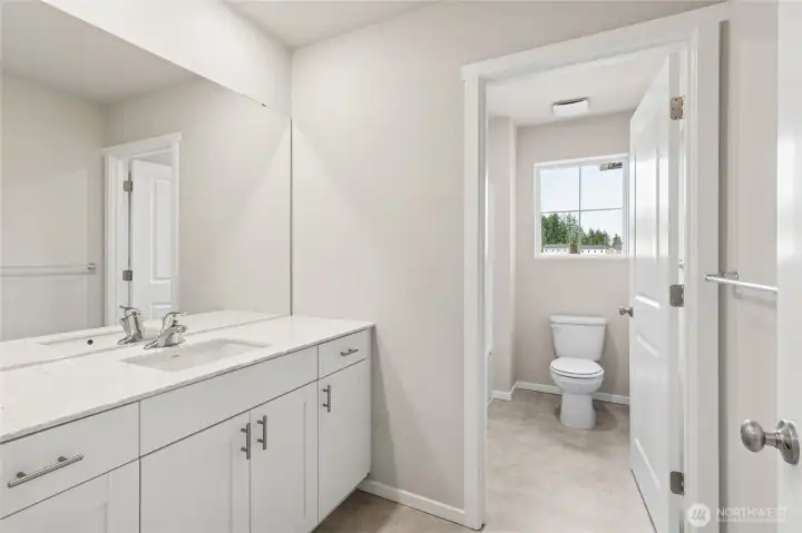 Spacious guest bathroom featuring a white vanity with quartz countertop, chrome hardware, a large mirror,  and a window providing natural light. Photos are representative only and may display different color packages and/or upgrades.
