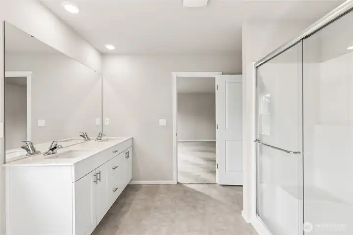 Primary bathroom showcasing the wide vanity, white quartz countertop, chrome faucets, large mirror, and a spacious walk-in shower with frameless glass doors. Photos are representative only and may display different color packages and/or upgrades.