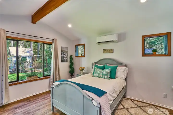 Cozy angle of the lower-level bedroom highlighting the vaulted ceiling, mini-split heat pump, and window that fills the space with natural light and garden views.