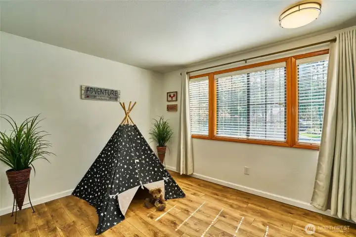 One of two upstairs bedrooms featuring laminate hardwood flooring and wood-wrapped windows. Currently staged as a playroom, this bright and versatile space is a true bedroom.