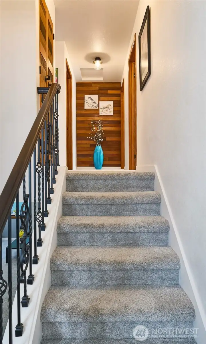 Newly opened stairwell featuring updated railings in place of the original pony wall for a more spacious feel. View also highlights the reclaimed wood accent wall at the end of the hallway, adding warmth and character.
