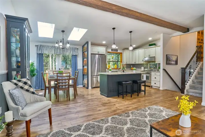 Corner view of the open-concept living area showcasing the flow between the living room, kitchen, and dining space, with stairways leading both up and down that enhance the home’s spacious, connected feel.