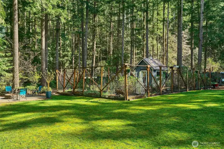 Peaceful backyard featuring a fully fenced garden with raised beds and a charming potting shed, surrounded by lush greenbelt forest. The fencing helps keep wildlife out of the garden while still allowing you to enjoy their visits throughout the yard.