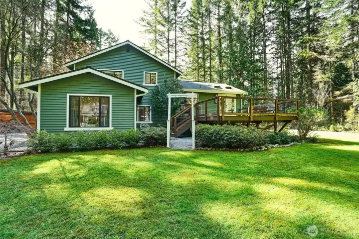 Rear view of the home highlighting the beautifully landscaped grounds and spacious deck—perfect for outdoor gatherings or peaceful relaxation amid nature.
