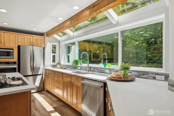Beautifully remodeled U-shaped kitchen showcases quartz countertops, exposed beam accent, and a stunning solarium-style wall of windows that floods the space with natural light. Beautifully remodeled U-shaped kitchen showcases quartz countertops, exposed beam accent, and a stunning solarium-style wall of windows that floods the space with natural light.