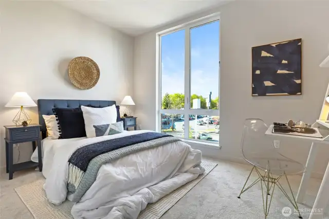 A sunlit bedroom designed for comfort, with oversized windows, plush carpeting, and space for a desk, is the perfect work-from-home or guest retreat.