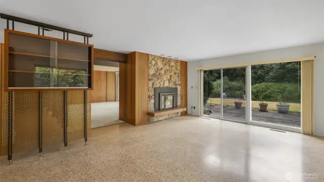 Family room features large windows, terrazzo floors, the other side of the dual fireplace and large siding doors that provide access to the large backyard.