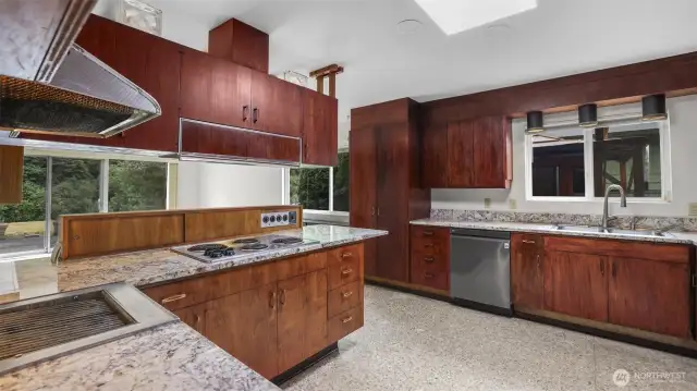 Kitchen features stainless steel appliances, terrazzo floors, warm cabinetry, and window above the sink.