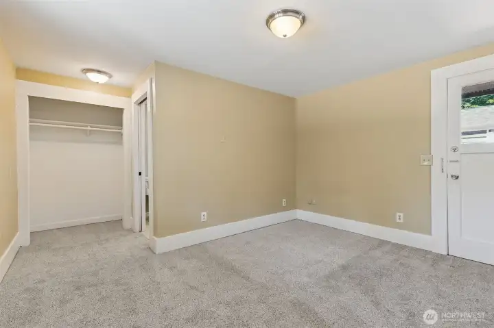 This is Unit A's main floor primary bedroom with the closet just ahead next to the 3/4 bathroom. The exterior door out the back deck is to the right.