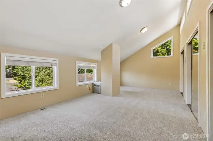 Upstairs in Unit A, this massive vaulted room is a blank canvas for whatever you envision. With oatmeal carpeting and warm-toned walls, it’s a cozy yet spacious area. A big window with wide slat blinds, along with an upper accent window in the vaulted area, fills the room with light. Three huge walk-in closets give you all the storage you need, and the space is large enough to fit multiple sleeping dorm-style bunks or serve as a massive rec room for gatherings. At the end of the upstairs room in Unit A, the open loft space overlooks the staircase, adding a sense of openness and light. A deep walk-in closet at the top of the staircase offers extra storage, while the carpeted stairs ensure safety, comfort, and a quieter feel. The mirrored closet door reflects light, making the space feel even more spacious and bright.