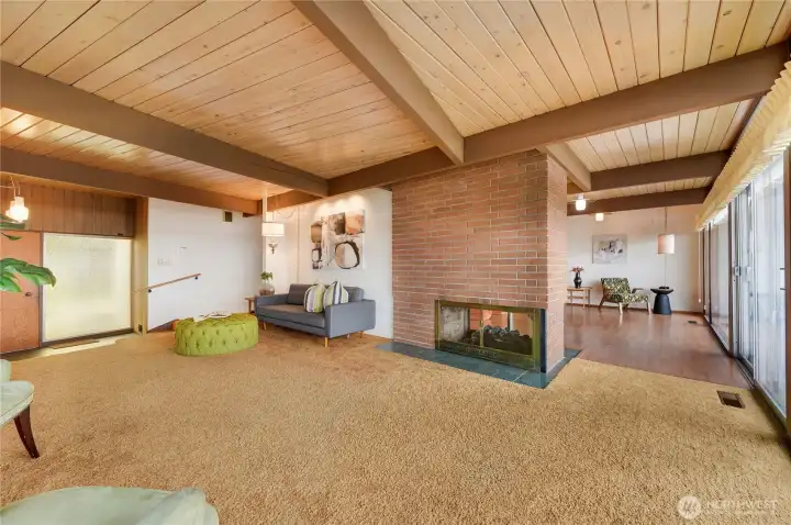 This striking living room blends iconic design with warm Northwest character. Exposed wood-beam ceilings, a dual-sided brick fireplace, and a sunken conversation area create an inviting, architectural focal point. Floor-to-ceiling windows flood the room with natural light, framing the surrounding landscape and enhancing the home’s seamless indoor-outdoor connection. Rich textures, retro accents, and thoughtful sightlines make this space ideal for both relaxed living and stylish entertaining—a timeless showcase of mid-century modern living.