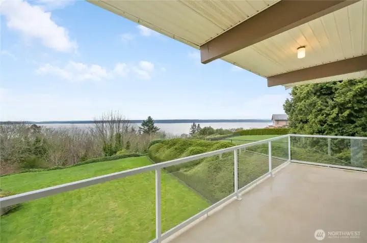 This covered view deck offers a peaceful vantage point overlooking lush greenery, sparkling water, and the distant mountains. Glass railing panels keep the scenery uninterrupted, creating a seamless connection to the outdoors. It’s the perfect place to unwind at the end of the day, with a front-row seat to watch the sky transform during gorgeous Northwest sunsets. A serene, year-round retreat that elevates the home’s indoor-outdoor living experience.