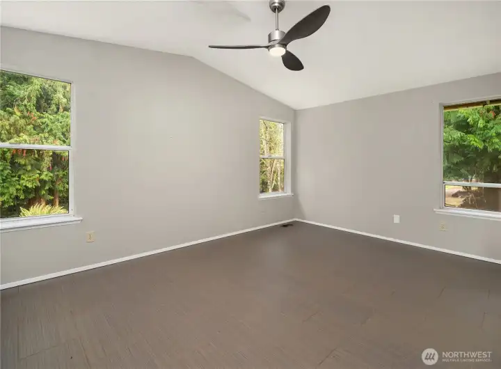 Spacious primary bedroom featuring a vaulted ceiling, modern ceiling fan, multiple windows, and updated tile flooring.