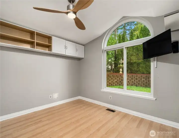 Enter a bright bonus room with hardwood floors, ceiling fan, plenty of built-in storage, and a stunning large arched window.