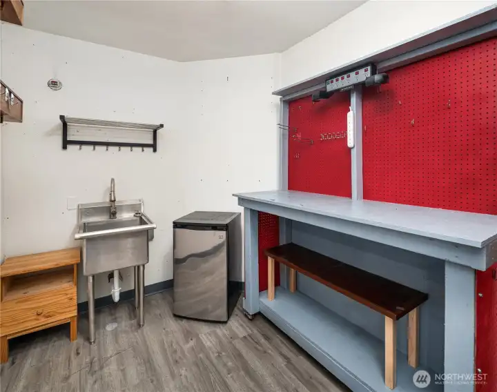 Utility/workshop area adjacent to the garage includes a stainless steel sink, mini fridge, large workbench with pegboard storage, and additional shelving.