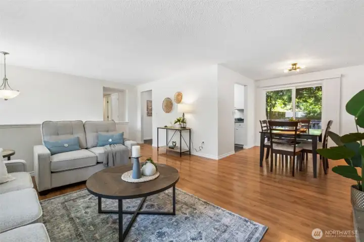 Light-filled open living and dining spaces feature warm wood-look flooring, a neutral palette, and sliding doors that bring in natural light and connect to the outdoor patio. The functional open layout offers comfortable everyday living and an inviting setting for entertaining family and friends.