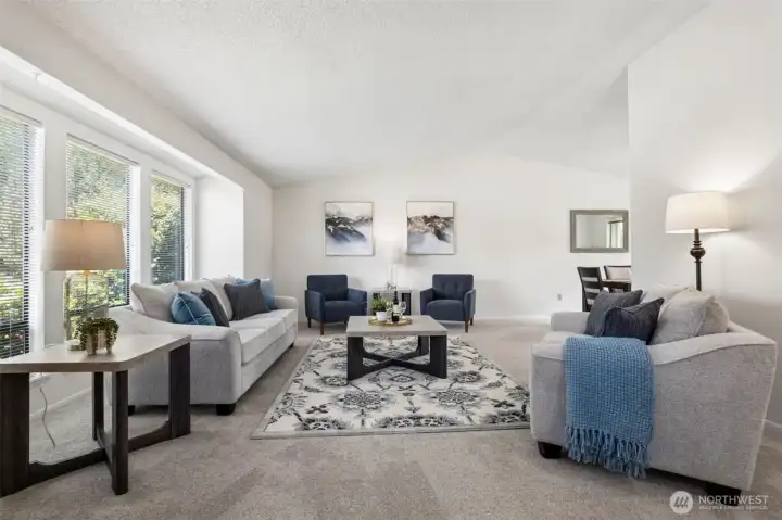 Bright and inviting living room featuring vaulted ceilings, expansive picture windows, and soft neutral finishes.