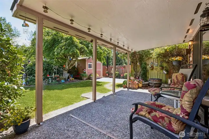Relax and unwind beneath the covered patio, a charming outdoor retreat complete with a soothing water feature, decorative garden accents, and peaceful views of the lush, fully fenced backyard.