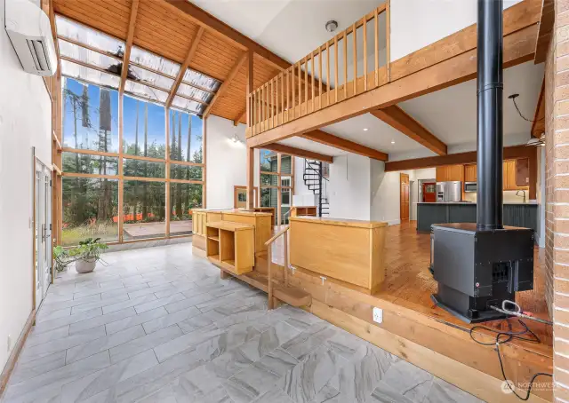 The great room is flooded with natural light from the floor-to-ceiling windows, showcasing elegant hardwood floors and a vaulted ceiling. The  fireplace and circular staircase create a cozy yet striking centerpiece.