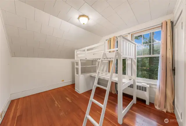 Bedroom with bunk-style bed, sloped ceiling, and a large window overlooking greenery.